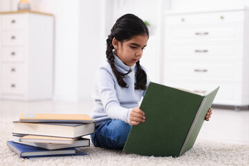 Fototapeta premium Cute little girl reading book on floor at home