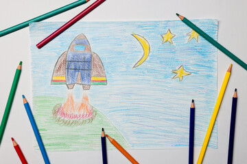 Beautiful child's drawing of rocket and pencils on white background, flat lay