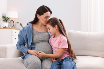 Obraz premium Pregnant woman and her daughter sitting on sofa at home