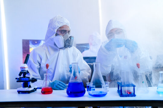 Virology researchers in full biohazard hazmat suits analyzing infectious pathogen samples. Biomedical scientists working in high-security BSL-4 containment laboratory.