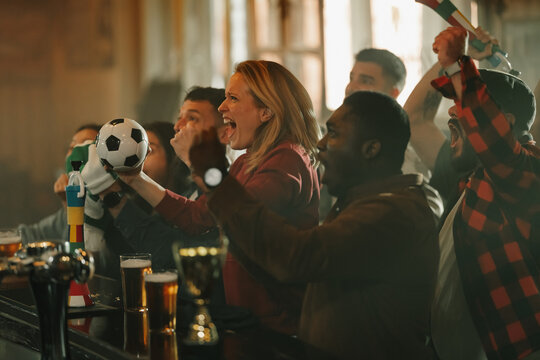 Diverse soccer fans cheering together celebrating goal in bar