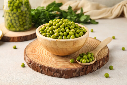 Wooden bowl and spoon with canned green peas on white background
