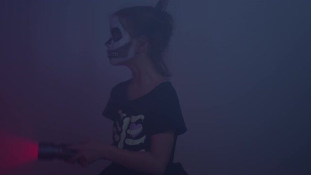Girl wearing skeleton costume and face paint holding torch. Zoom in shot of little child looking towards camera with spooky expression creating Halloween mood