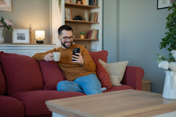Obraz premium Man relaxing on sofa enjoying smartphone content