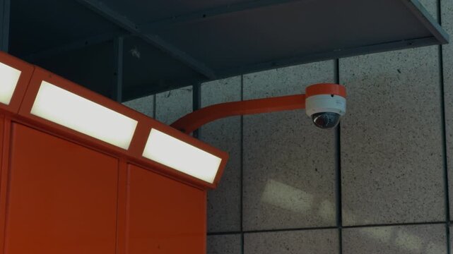 Ceilingmounted dome camera over station surface. Modern transit station with backlit panels and safetyfocused surveillance system
