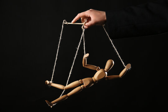 Hand of puppeteer manipulating marionette on black background