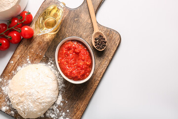Fototapeta premium Board with raw dough, bowl of tasty tomato sauce and ingredients on white background