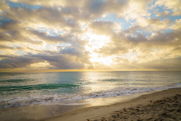 Fototapeta premium Golden sunrise rays reflecting on wet beach sand and gentle ocean waves during a calm morning on the coast of Hollywood, Florida.