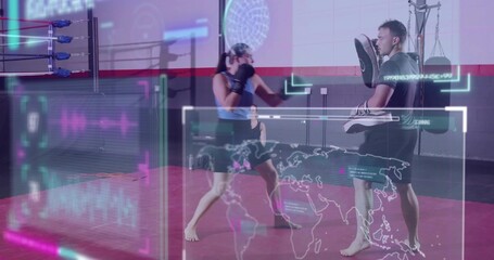 Punching female boxer wearing tank-top, gloves hitting coach holding focus-pads at gym, AR overlays