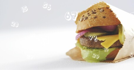Displaying wrapped burger sitting on studio tabletop with seeded bun, numeric overlays, copy space
