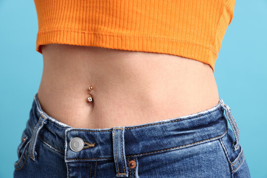 Woman with belly button piercing on light blue background, closeup