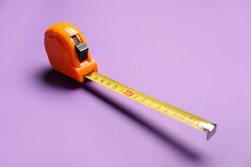 Orange measuring tape on violet background, closeup