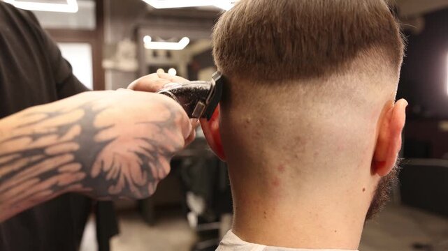 Stylist cutting man's hair with clipper in barbershop, closeup