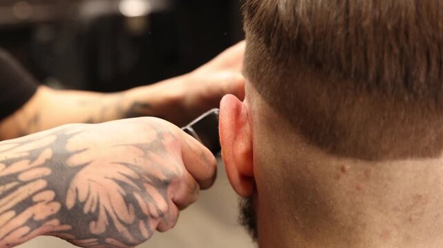 Stylist cutting man's hair with clipper in barbershop, closeup