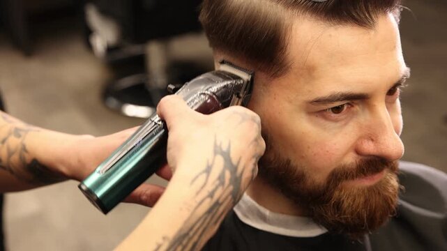Stylist cutting man's hair with clipper in barbershop, closeup