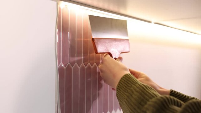 Woman applying peel and stick tiles on wall in kitchen, closeup