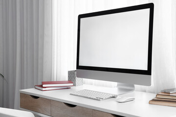 Blank computer monitor with stationery on desk near window in room