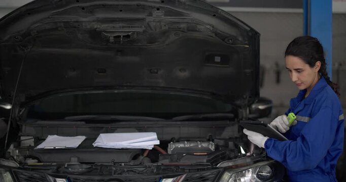 Mechanic use vehicle's onboard diagnostic tool to identify error codes in automotive workshop. Focusing intently on tablet device, showcasing modern diagnostic techniques and technical expertise.
