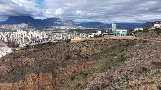 Rocky Hillside Foreground Overlooking Distant City And Mountain Range, Sparse Scrub Vegetation, Exposed Soil