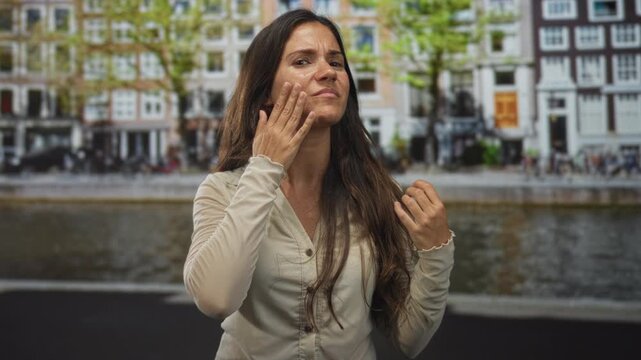 Woman touching hair and face on an amsterdam canal street, grimacing while checking her cheek; irritation treatment.