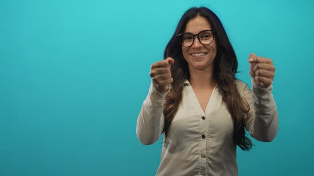 Woman smiling, miming driving with clenched hands and steering gesture in teal studio set; playful confidence.