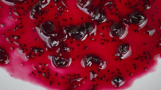 Rich textured currant spread with shiny berry fragments and seeds. Detailed macro photograph highlighting smooth syrupy currant jam with seed particles on clean white surface