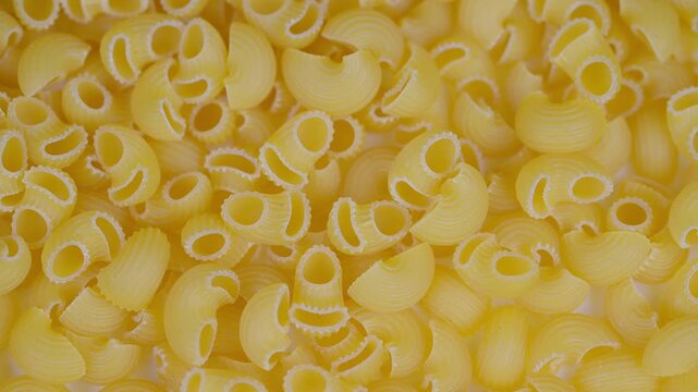 Uncooked durum wheat pasta shells. Golden ridged pasta shells in detailed pattern. Closeup of textured dry pasta shells with ridges and warm tones ideal for culinary visuals