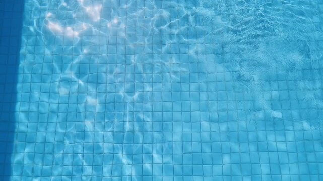 Clear blue swimming pool water surface with gentle ripples and sunlight reflections over tiled bottom