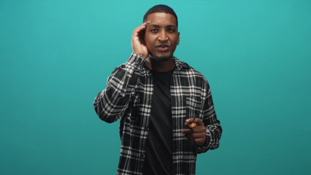 Man holding screwdriver in right hand, hand to ear listening gesture, wearing plaid flannel shirt in studio; curiosity problem solving focus.
