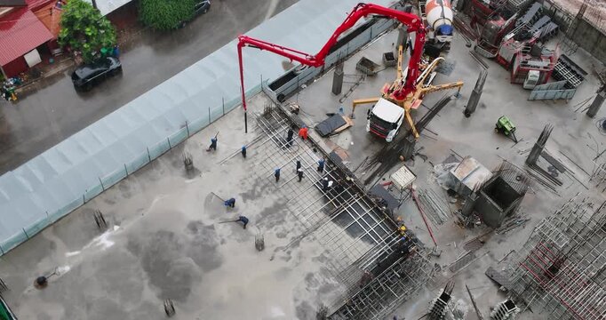 Aerial view of a construction site, workers pouring concrete with red pump truck during rain.