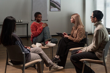 Group of adults and one Black gen Z girl sitting in circle engaging in discussion during support...