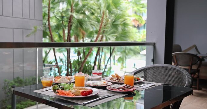 Luxurious breakfast spread with fresh orange juice, omelets, and tropical fruits, served on a private balcony overlooking a resort pool and lush palm trees. A concept of luxury vacation, healthy
