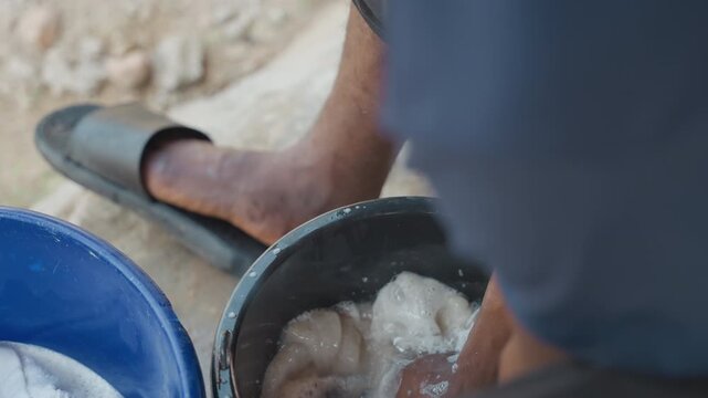 Washing clothes outdoors in sunlight. Practical household task of washing and wringing clothing outdoors. Performing daily house chores of rinsing and squeezing garments in sunlight for cleanliness