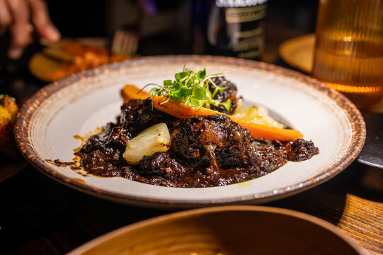 Hearty portion of dark braised meat stew with tender carrots and onions, garnished with fresh microgreens, creating a savory dining experience on a rustic ceramic plate