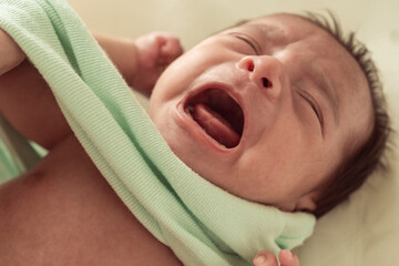 Newborn baby crying while being dressed at home. Concept of daily routine, infant discomfort and parenting challenges.
