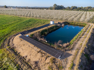 Sustainable Farming Innovation: Wide aerial perspective of a solar-powered irrigation system and blooming almond orchard.