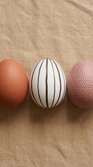 Obraz premium Three decorated eggs on beige linen, minimalist overhead still life for Easter and spring celebration, soft neutral palette for food styling and craft design