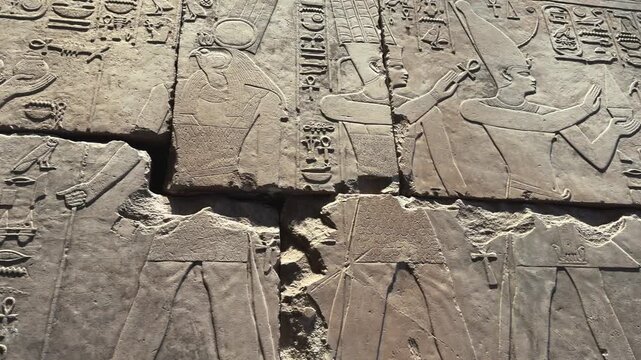 Close up of carved cracked stone wall relief with priests, pharaoh and the God RA. Cinematic panoramic motion shot