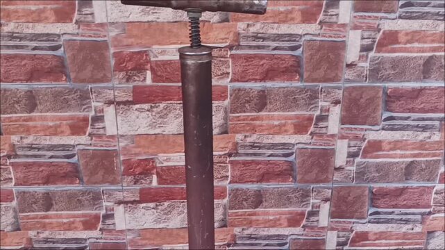 Footage of an antique metal manual air pump with a red pressure tank and rubber hose, placed on a rustic-style stone wall
