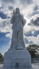 The famous sculpture of Christ of Havana. A tall statue made of white carrara marble against a background of blue sky and clouds. The pedestal is enclosed by a latticed fence. Cuba. Havana.   

 