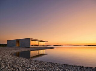 Fototapeta premium Modern concrete house on a pebble beach at sunset with large glass windows reflecting the golden sky