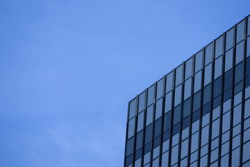 Fototapeta premium A section of a modern building with many rectangular glass windows reflecting the clear