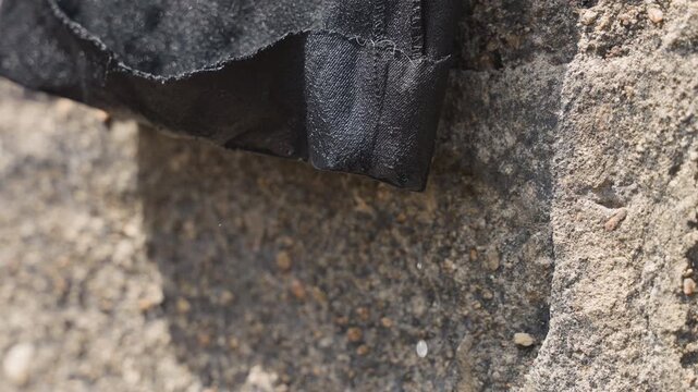 Closeup black fabric on house wall showing rough stone texture, dusty pebbles, subtle shadow, sunlight highlight, tactile fibers and weathered surface suggested plot mason inspecting exterior wrap