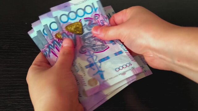 Hands counting ten thousand Kazakhstan tenge banknotes. Close up of female hands rapidly counting a stack of Kazakhstan currency on a dark table. Business concept for cash payment and financial accoun