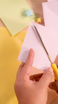 Vertical Close Up of Hands Cutting Pastel Paper for Origami Craft