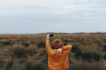 Woman lifestyle concept showing a person in a brown jacket and hat taking a selfie in a natural...