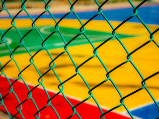 View through green chain link fence of colorful outdoor basketball court with painted lines and...