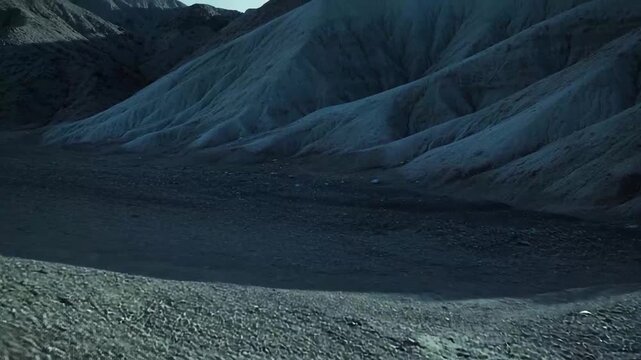 Sweeping view of a vast desert landscape featuring barren, eroded mountains and rippled terrain under the dim light of dusk, conveying wilderness and desolation