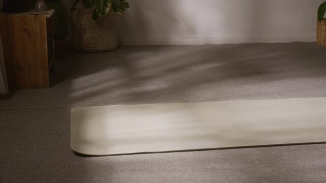 Medium tracking shot of young female yoga practitioner squatting down and rolling out mat on floor with camera following, suggesting motivation, positive energy and enthusiasm