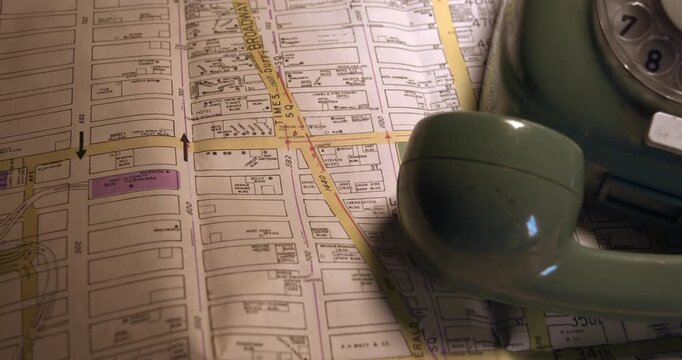 Smooth camera move revealing a retro green dial phone resting on a New York paper map. Crime detective, travel planning or noir investigation.